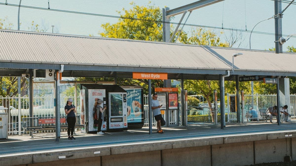 People waiting at West Ryde train station platform under clear skies, capturing daily commutes.