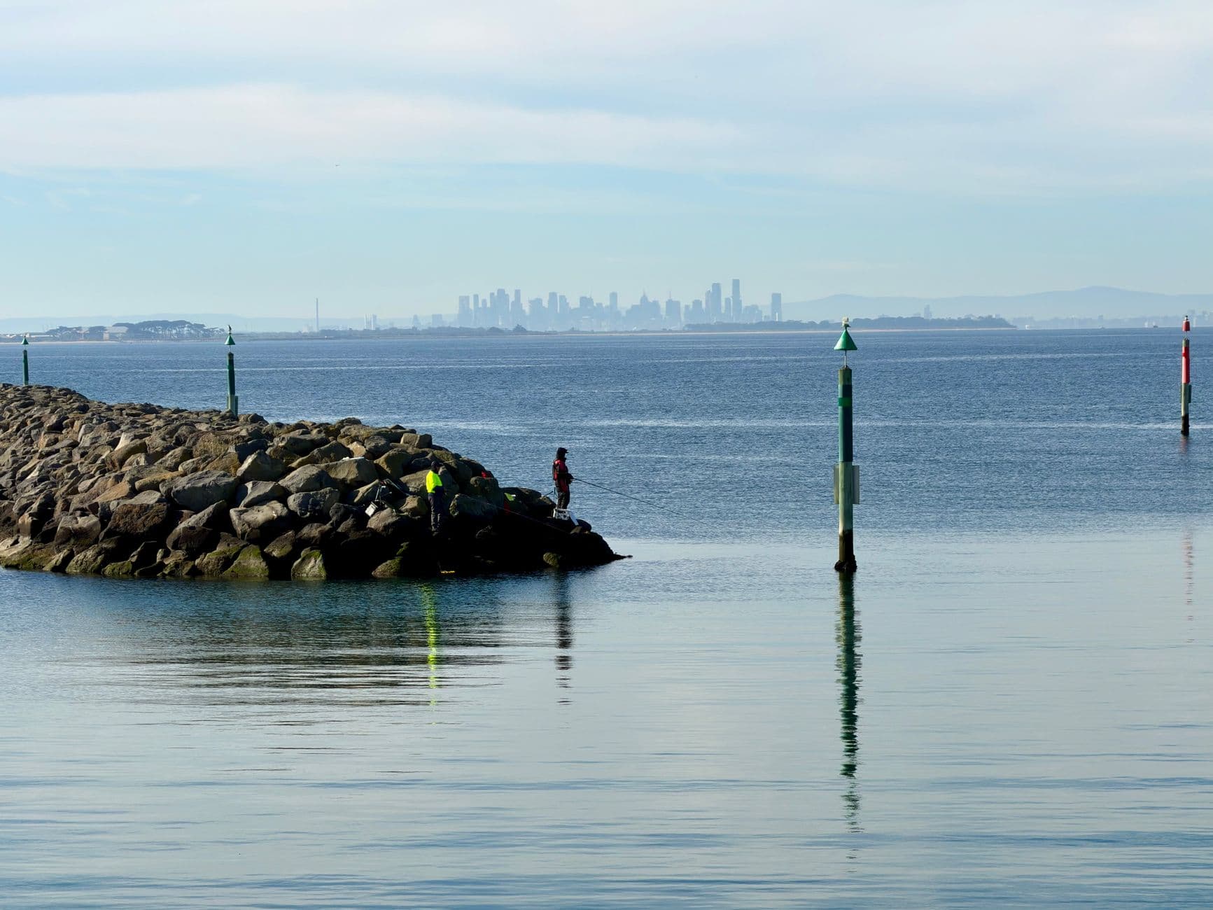 Tranquil view of Melbourne skyline from Werribee South with fishing on the rocky shore.