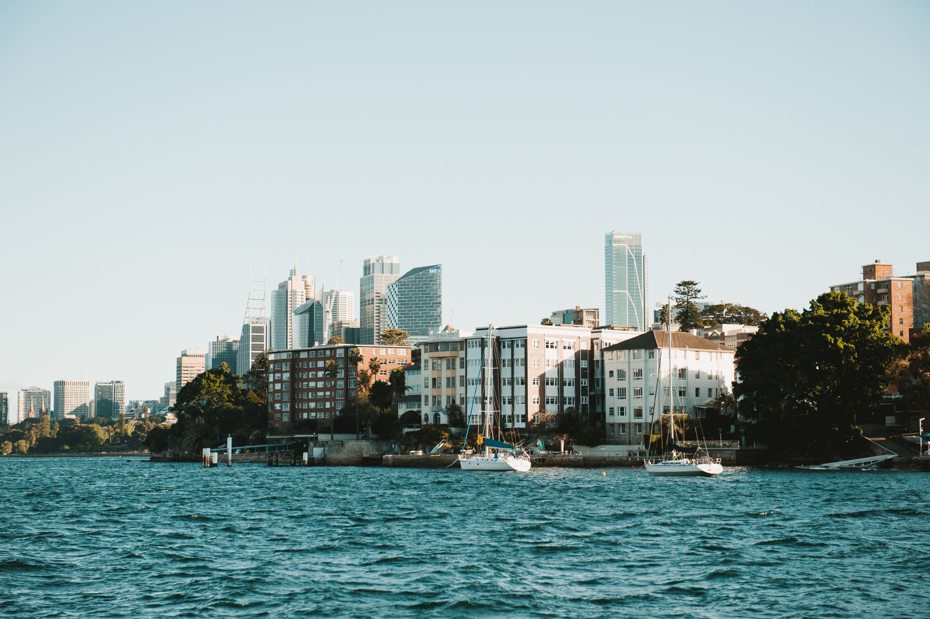 Scenic view of Sydney skyline across the water with boats in the foreground, highlighting urban architecture.